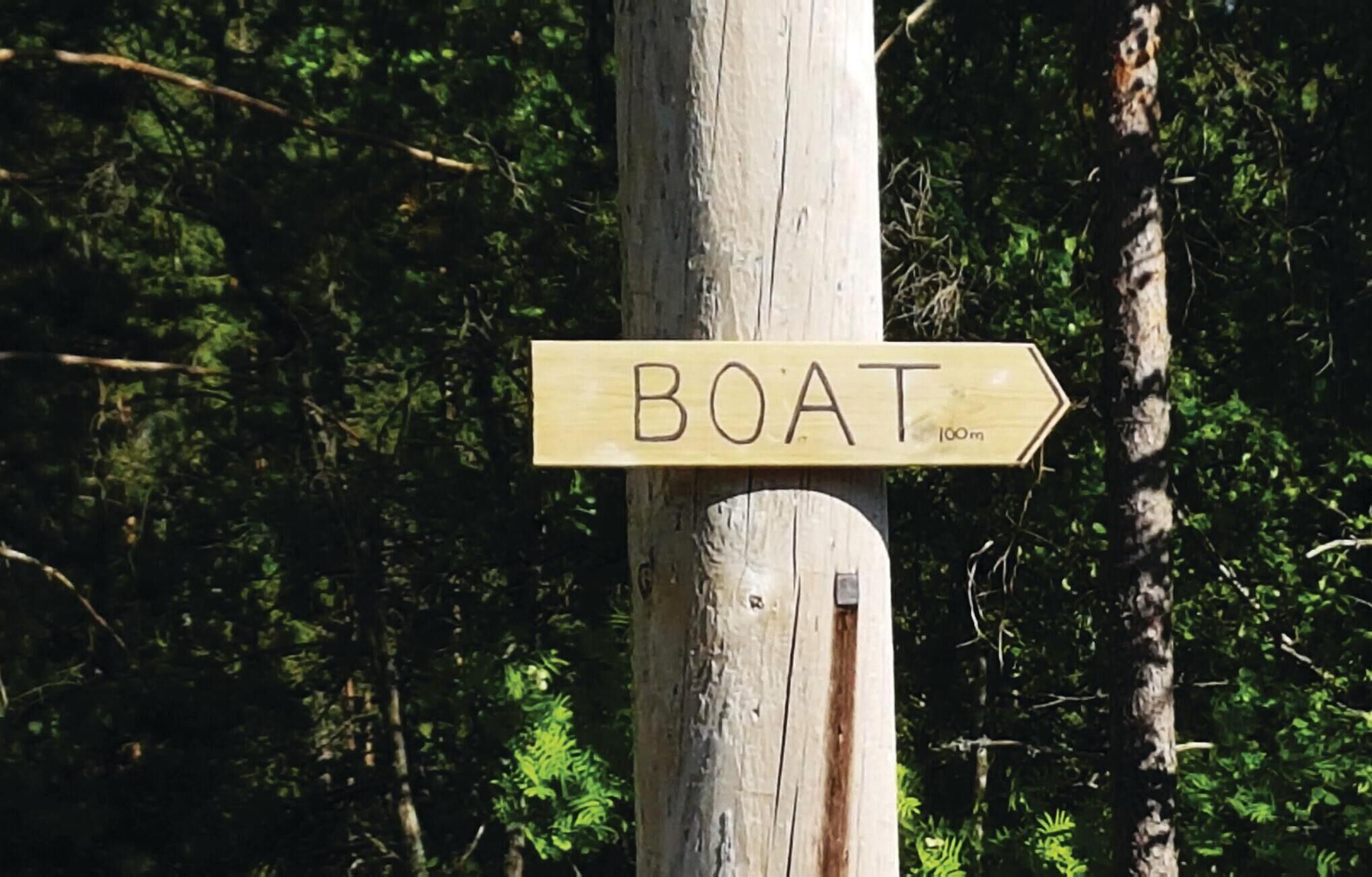 Ein hölzernes Wegweiser mit einem 'BOOT'-Schild, das nach rechts zeigt und eine Richtung anweist.