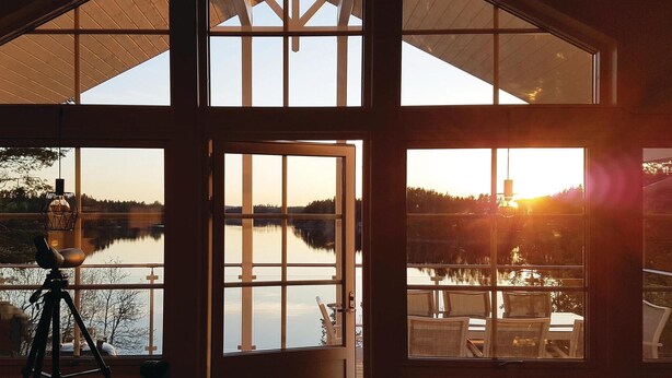 A room with large windows overlooking a lake, a tripod, and a chair. - Gorgeous home in årjäng with WiFi (Årjäng)
