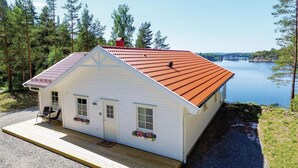 A white cabin with a red roof, wooden deck, and flower boxes, located near a lake. - Gorgeous home in årjäng with WiFi (Årjäng)