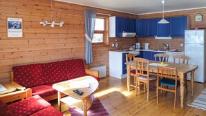 Een gezellig houten interieur met een eethoek, een tafel, stoelen, een keuken met blauwe kastjes en een rode bank.
