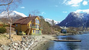 Een geel huis met een rood dak aan een meer, omringd door bergen en een steiger.