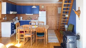 Een kleine keuken met houten kastjes, een eettafel met stoelen, een fornuis en een koelkast.
