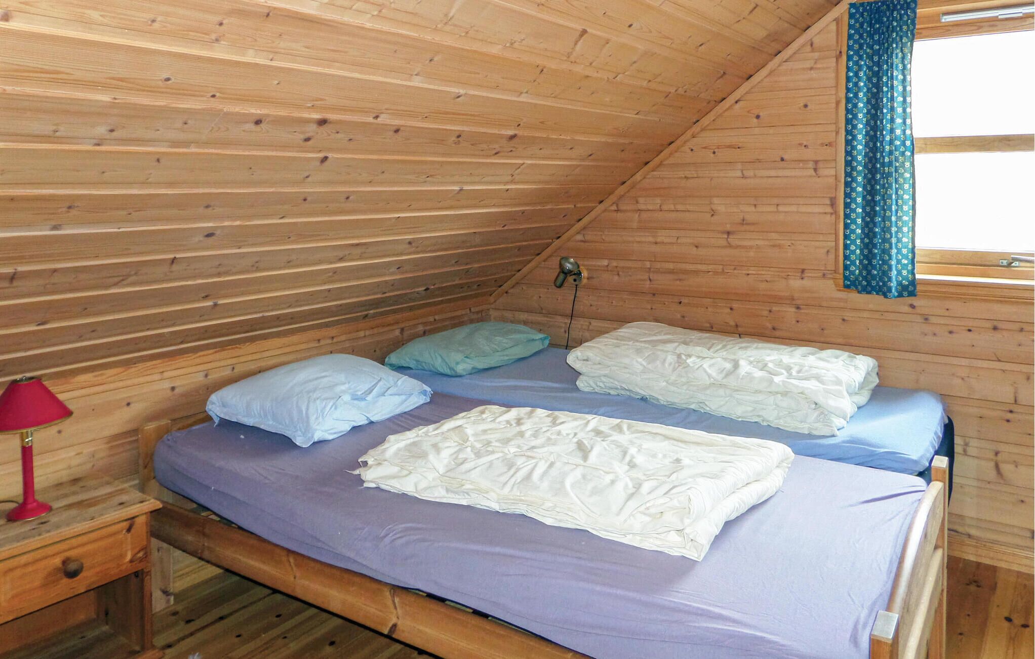 Una cama individual con cabecera de madera en una habitación tipo cabaña con techo inclinado y paredes de madera.