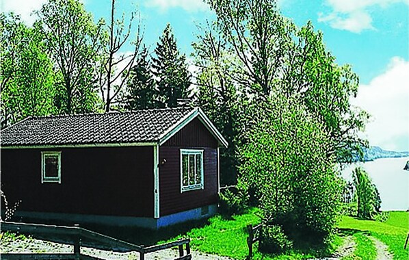 A small, dark-colored cabin with a sloped roof, situated next to a body of water and surrounded by trees. - Cozy home in Dingle with WiFi (Dingle)
