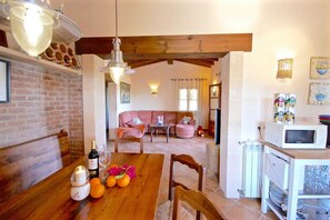 A cozy living area with a wooden dining table, a sofa, and a kitchen area with a microwave. - 44252 Finca Son Homar (license number ET / 3279) - 44252 Finca Son Homar (Petra)