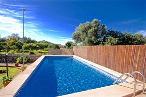 Une piscine rectangulaire à l’eau d’un bleu limpide, entourée d’une clôture en bois et d’un mur de pierre.
