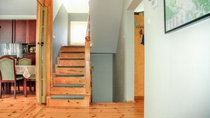 Un escalier en bois menant à un deuxième étage, un coin repas avec une table et des chaises, et une carte accrochée au mur.