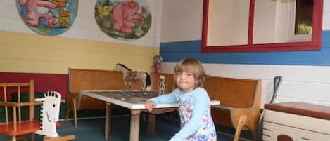 Un niño en una sala de juegos con un banco de madera, una mecedora y una pequeña mesa.