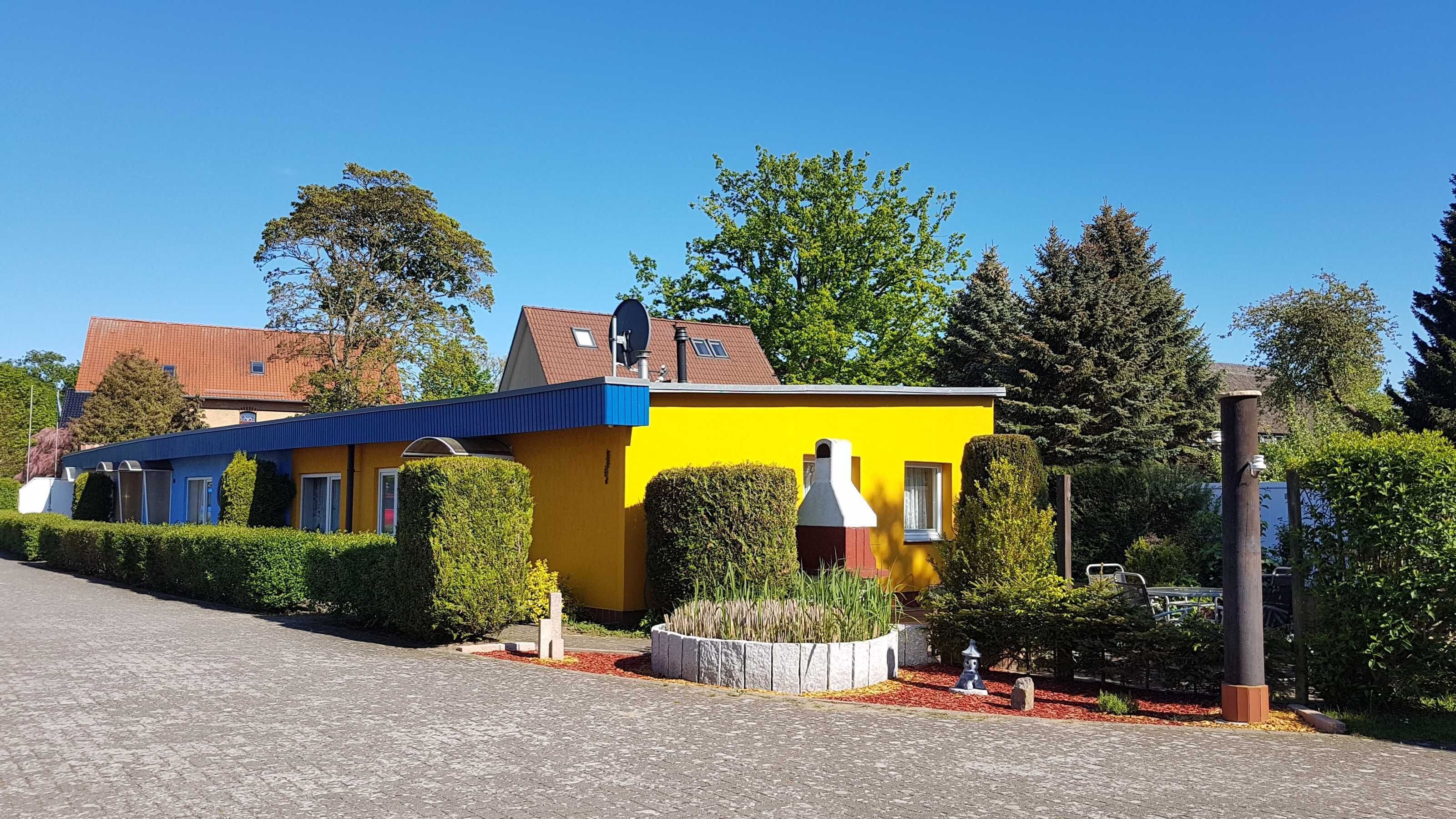 A two-story building with a yellow facade and blue roof, surrounded by well-maintained hedges and trees.