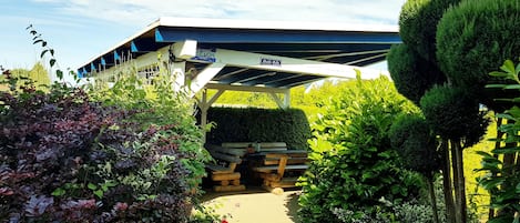 Een overdekt buitengebied met een bord voor 'Grill-Roet' en een stapelhout.