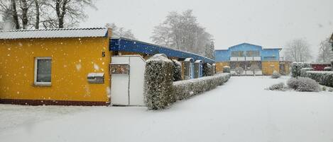A snow-covered outdoor area with a yellow building, a blue structure, and a white building in the background.