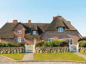 Een groot, traditioneel huis met bakstenen muren, een rieten dak en een stenen muur rondom het terrein.