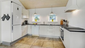 A modern kitchen with white cabinets, a black countertop, and a wooden ceiling. There are two windows with potted plants, a sink, and a stove. - Beautiful home in Herning with kitchen (Herning)
