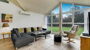 A spacious living room with a grey sofa, a black coffee table, and a beige armchair. There is a large window providing a view of the outdoors. - Beautiful home in Herning with kitchen (Herning)