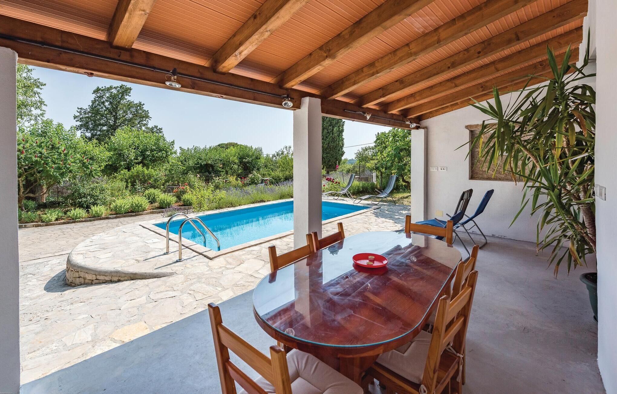Un'area esterna coperta con piscina, un tavolo e sedie, e vista su piante.
