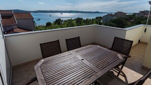 A wooden table with four chairs on a balcony overlooking a body of water with boats and buildings in the distance. - Holiday apartment with sea view (Biograd na Moru)