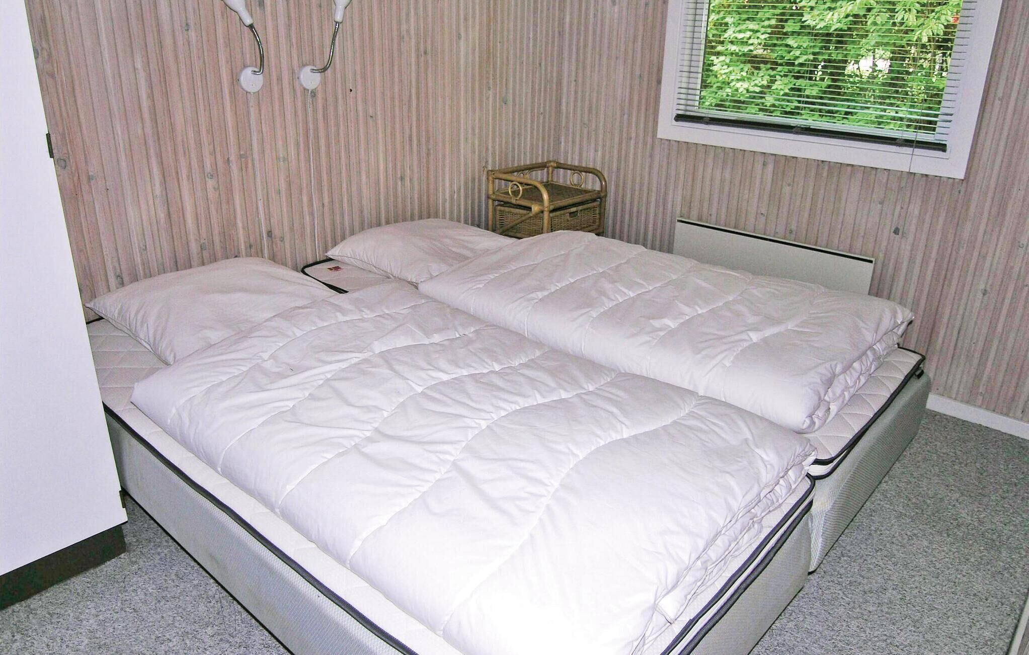 A double bed with white bedding in a room with striped wallpaper and a window with blinds.