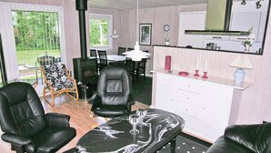 Un salon comprenant un canapé en cuir noir, un fauteuil en cuir noir, une table basse en cuir noir avec un plateau en verre, et un coin repas avec une table et des chaises.