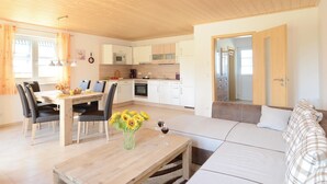 Uma sala de estar moderna com sofá, mesa de jantar com cadeiras e área de cozinha com armários e eletrodomésticos.