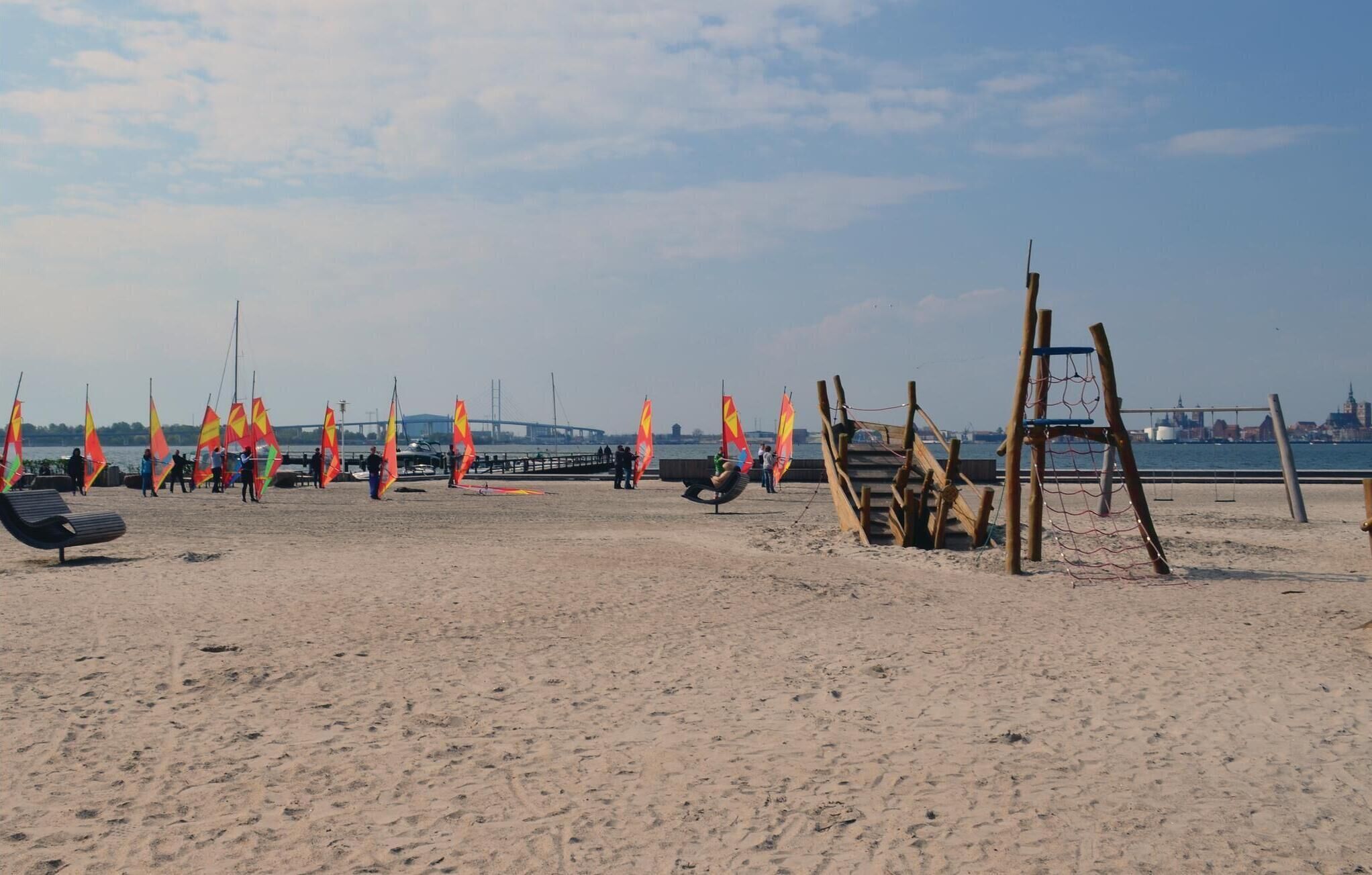 A sandy beach with windsurfing equipment and a wooden structure.