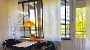 Una habitación con una mesa, dos sillas, una lámpara y un ventanal con persianas.
