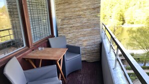 Un balcón con una mesa y dos sillas, una pared con textura y vistas a agua y vegetación.