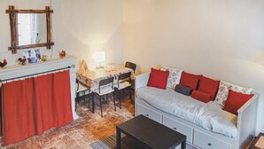 A cozy room with a dining table, chairs, a sofa with red and grey cushions, a small black table, and a red curtain.