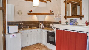 A kitchen with white cabinets, a red curtain, a clock, and a rooster decoration on the wall.