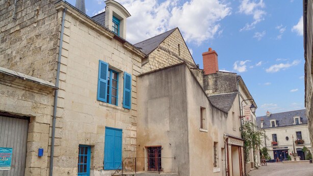 A historic building with a stone facade, blue shutters, and a staircase leading to an upper level.