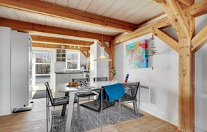 A modern kitchen with white cabinets, a dining area with a white table and black chairs, and a colorful abstract painting on the wall. - Cozy home in Blåvand with WiFi (Blåvand)
