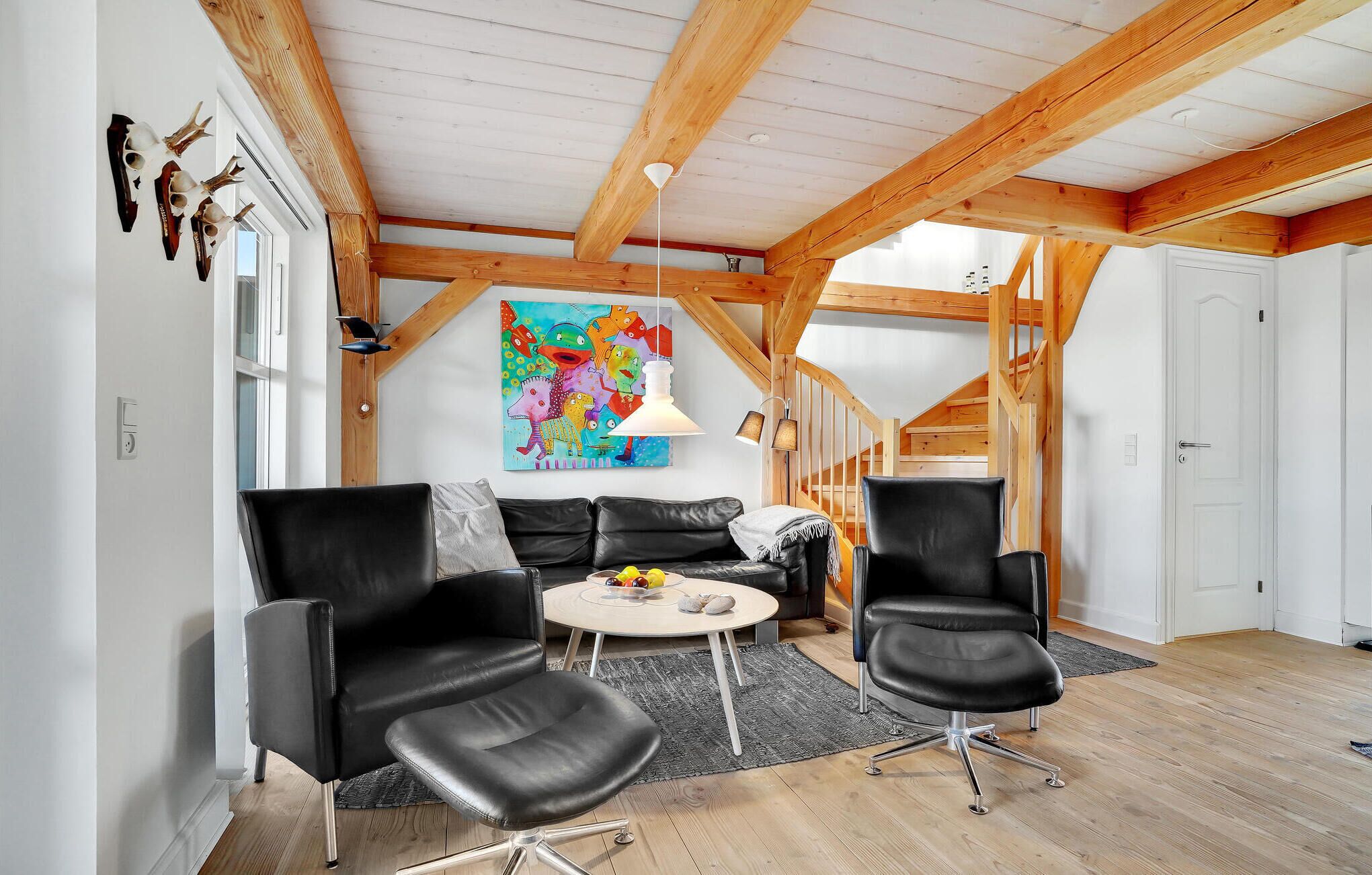 A modern living room with a loft-style ceiling, a colorful abstract painting, and a cozy seating area with leather chairs and a round table.