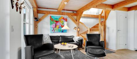 A modern living room with a loft-style ceiling, a colorful abstract painting, and a cozy seating area with leather chairs and a round table.