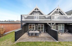 A two-story building with a balcony, a patio area with a table and chairs, and a barbecue grill. - Cozy home in Blåvand with WiFi (Blåvand)