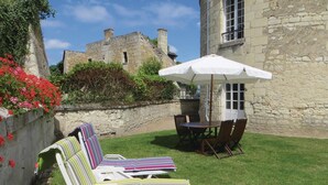 A courtyard with a stone building, a table with chairs, and striped lounge chairs.