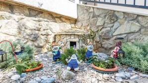 Un jardin avec des murs en pierre, une petite cabane et des statuettes de nains de jardin.