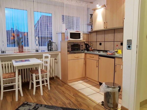 A compact kitchen with a dining area, a microwave, a kettle, and a trash bin.