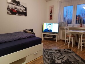 A bedroom with a bed, a desk, a television, and a window with curtains.