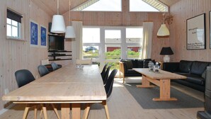 A spacious room with a large wooden table, a sofa, and a TV. There are windows allowing natural light and a view of the outside. - 3 bedroom beautiful home in Fanø (Fanø)