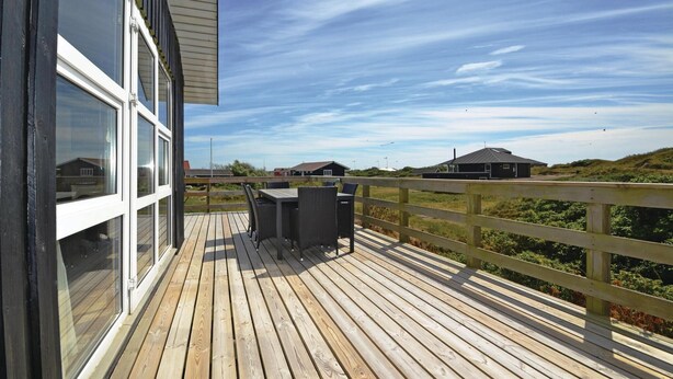 A wooden deck with a table and chairs, overlooking a coastal landscape with buildings and a clear sky. - 3 bedroom beautiful home in Fanø (Fanø)