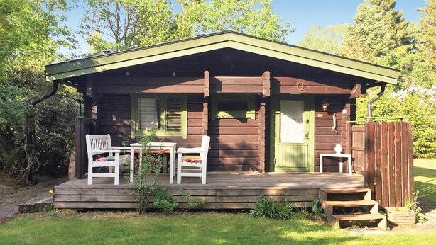 Eine rustikale Holzhütte mit Veranda, zwei weißen Stühlen und einem kleinen Tisch.