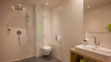 Une salle de bain moderne avec une douche à parois de verre, des toilettes blanches et un lavabo surmonté d’un miroir.