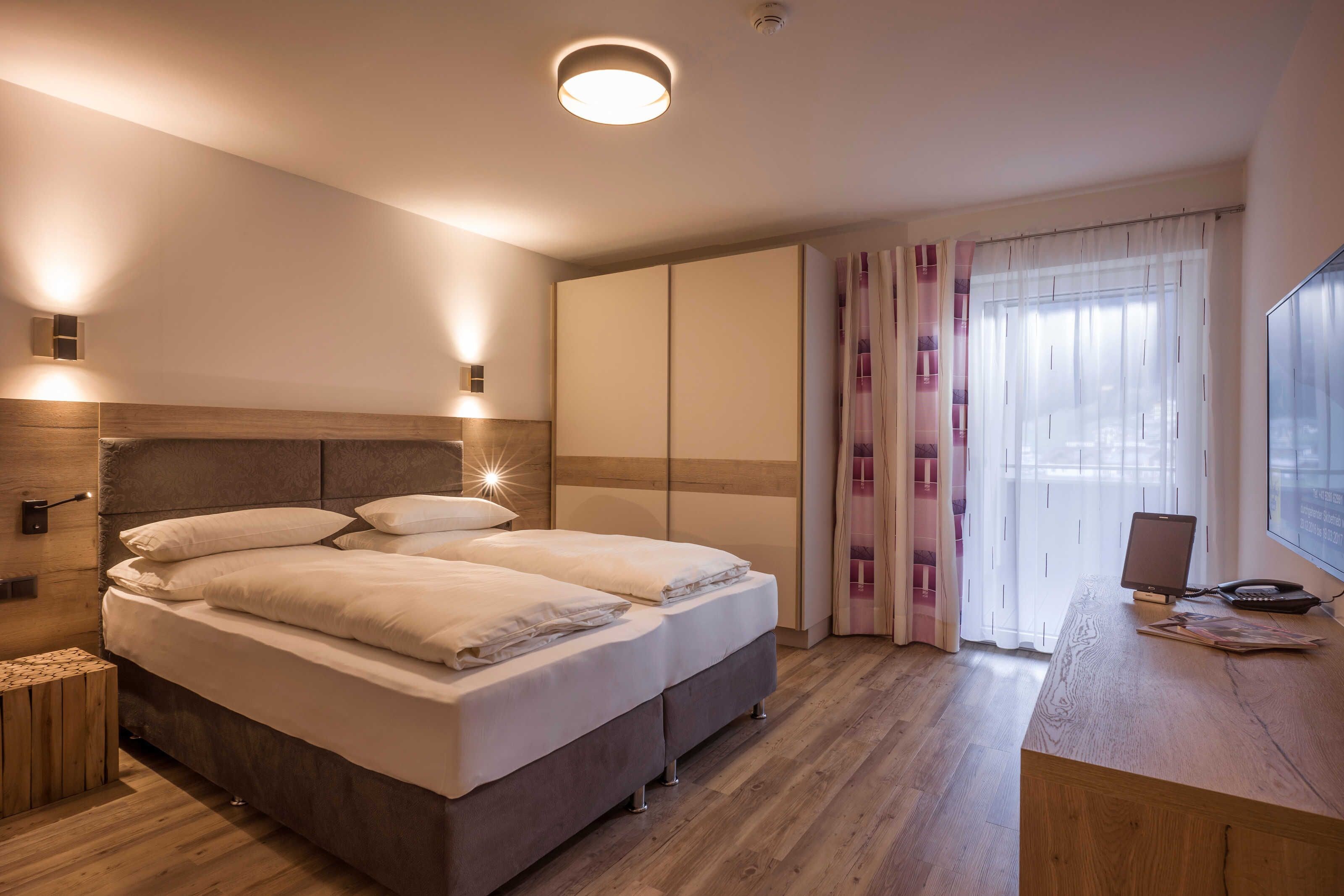 Ein Schlafzimmer mit Bett, Nachttischen, einem Schreibtisch mit Computer und einem Fenster mit Vorhängen.