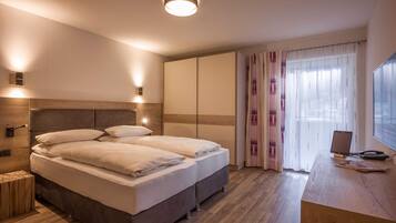 Ein Schlafzimmer mit Bett, Nachttischen, einem Schreibtisch mit Computer und einem Fenster mit Vorhängen.