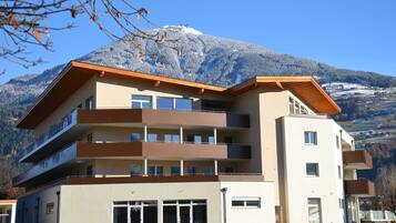 Ein mehrgeschossiges Gebäude mit Balkonen, einer flachen Dachterrasse und einem Blick auf die Berge.