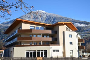 Ein mehrgeschossiges Gebäude mit Balkonen, einer flachen Dachterrasse und einem Blick auf die Berge.
