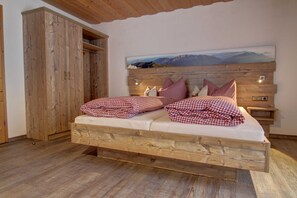 A wooden bed with checkered bedding, a wooden wardrobe, and a mountain landscape painting on the wall.