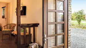 Une porte en bois avec des panneaux de verre dépoli, une chaise en osier, une petite table et un mur de pierre visible à travers la porte.
