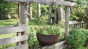 Une clôture en bois rustique, ornée d’un pot en métal suspendu, le tout entouré d’une végétation luxuriante.