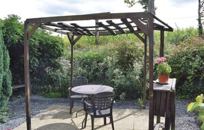 A wooden pergola with a round table and two chairs underneath.