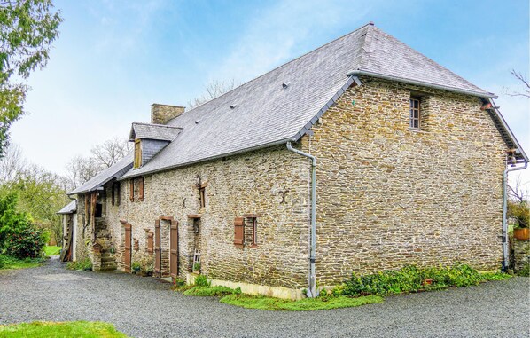 A stone building with a sloped roof, wooden shutters, and a gravel driveway.